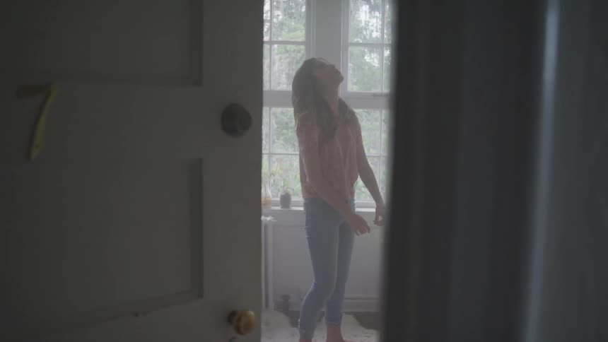 A teenager stands in a room and looks up at the ceiling