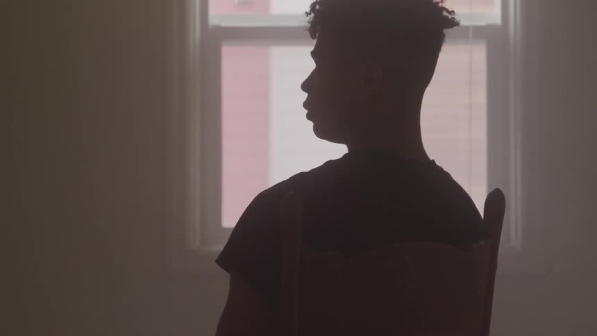A young black man sitting in chair before a window
