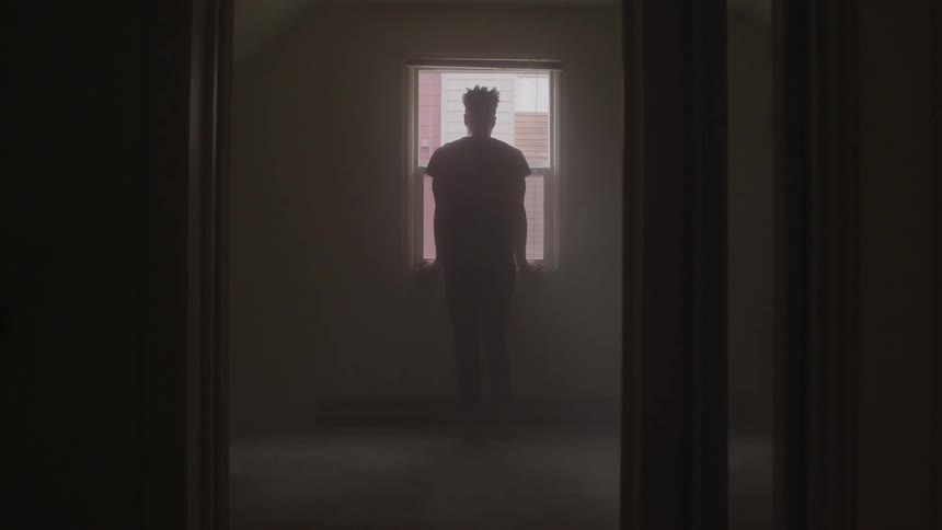 Man standing inside house looking outside through window