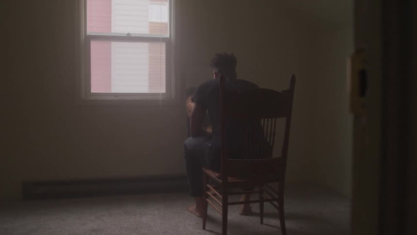 A person sits on a chair in a plain room by themselves