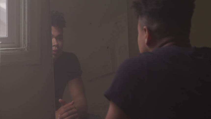 A black teen looks in a mirror and hangs his head down