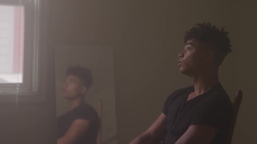 A young black man sitting in a chair in an empty room