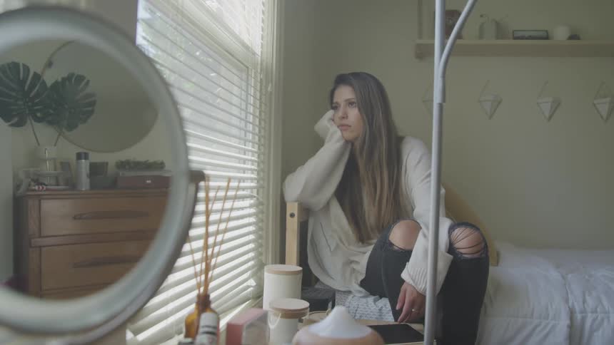 Woman sitting on bed looking outside through window