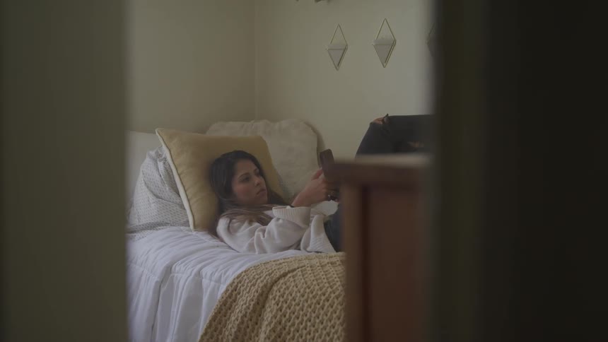 A young girl lies in bed and uses her smartphone