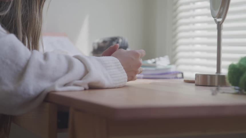 Brunette woman sitting at the table clasps hands in the studying room