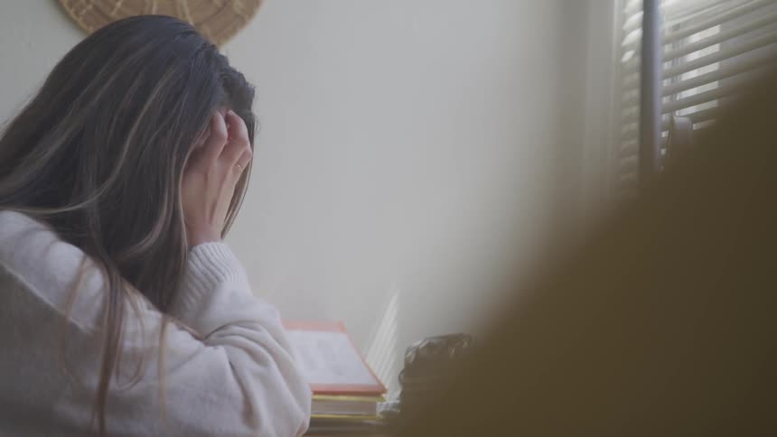 Brunette woman sitting at the table puts her hands on her head with a great sadness in the studying room