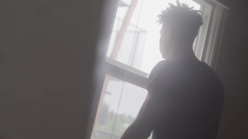 Man standing inside house looking outside through window