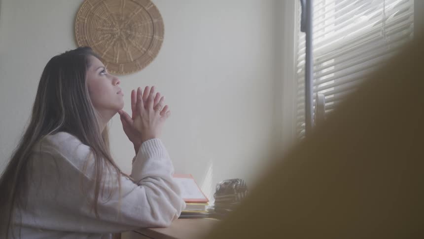 Brunette woman sitting at the table looks out the window and looks worried in the studying room