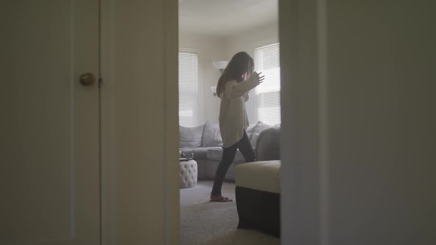 A young woman stressfully running a hand through her hair as she walks through a room talking on a smartphone