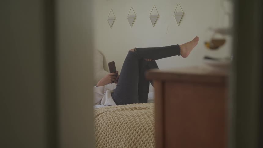 Woman lying on the bed uses smartphone in a room