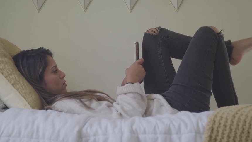 A woman lays on her bed using a cell phone