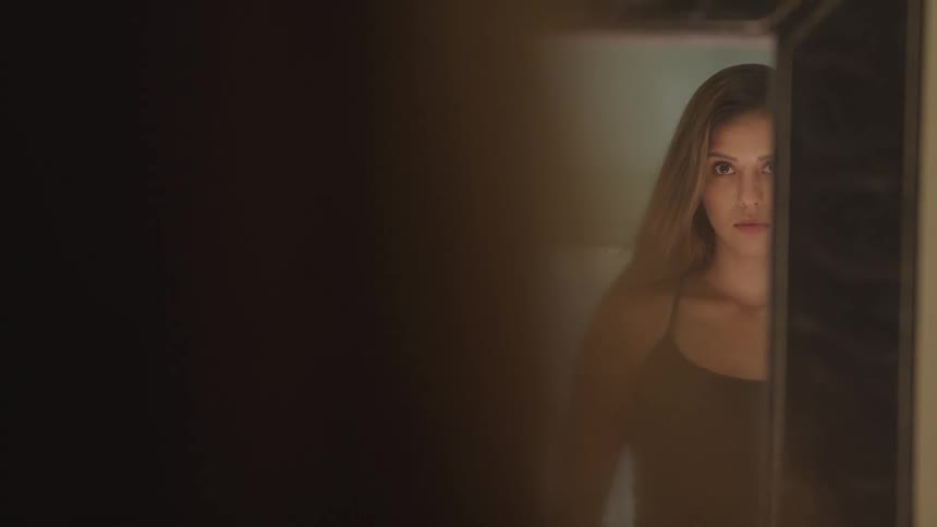 A female looks up from the floor and into a mirror as she stands under a light source