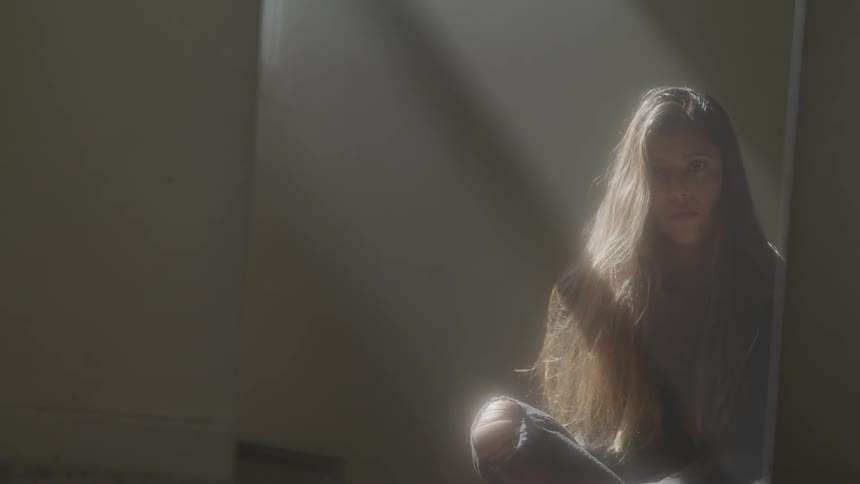 A long haired young woman with ripped jeans sits on the floor