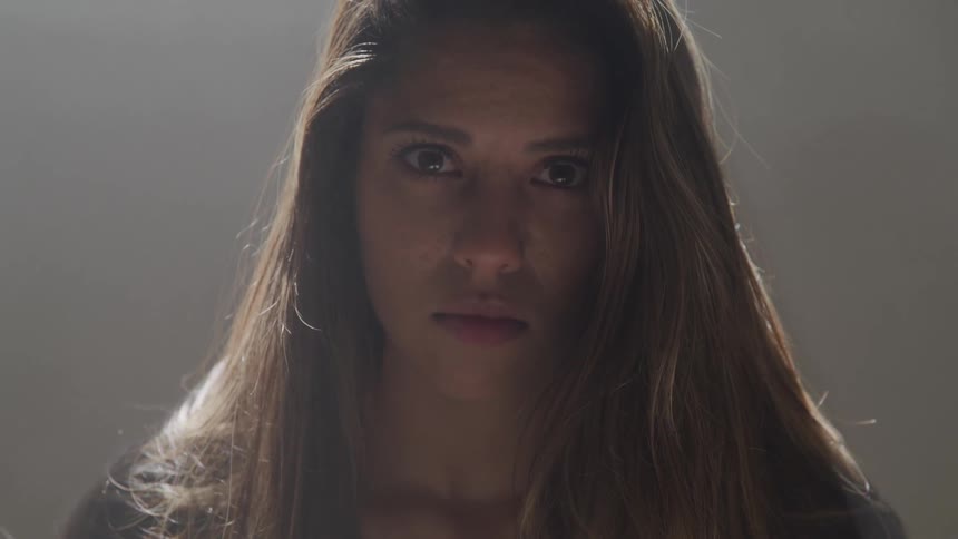 Brunette woman raise her head and looks at the camera while the sun shines through the hair