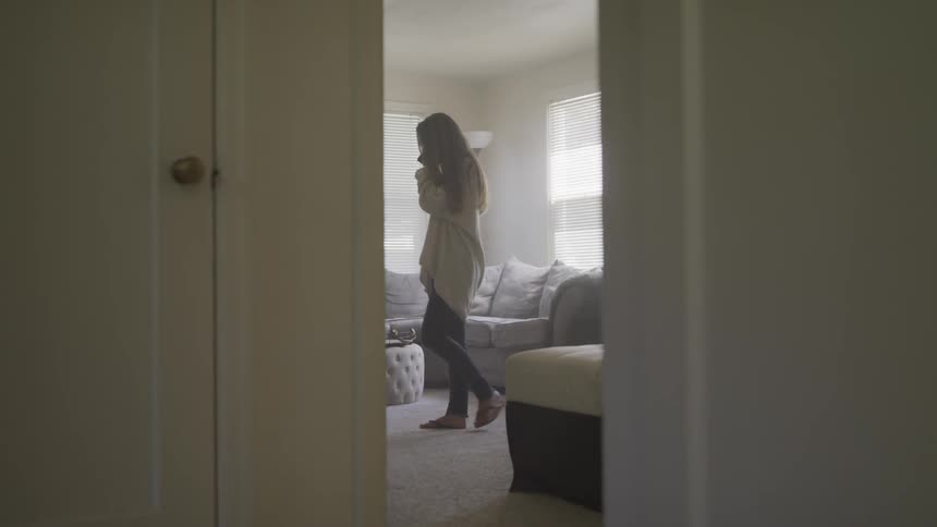 A young girls walks across a room as she talks on a phone