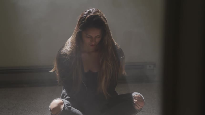 A teenager sits cross legged on the floor and looks down at the ground