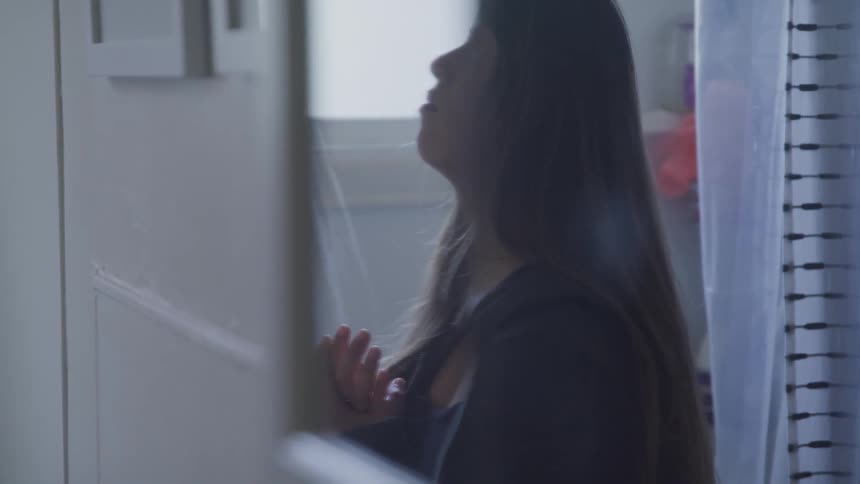 A woman is looking in the mirror as the shower runs