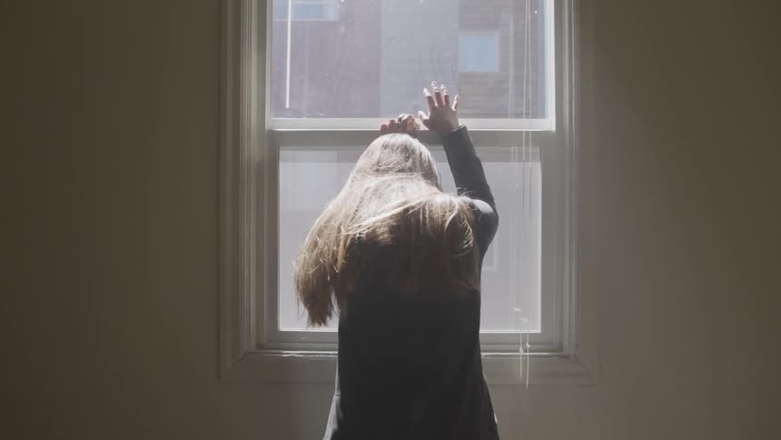 A young girl leans on a window with her head down