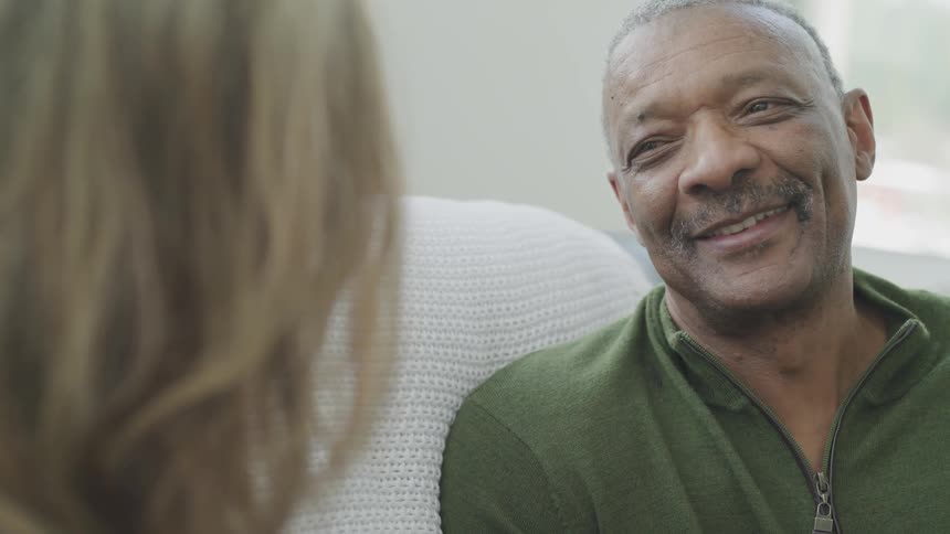 A man smiles while sitting next to and looking at a woman