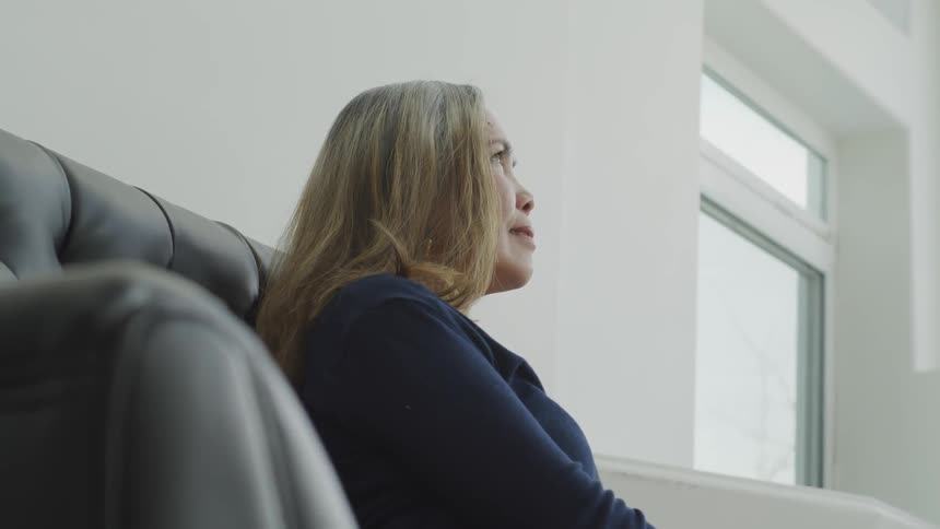 Blonde woman sitting on the black sofa looks up and smiles in a room
