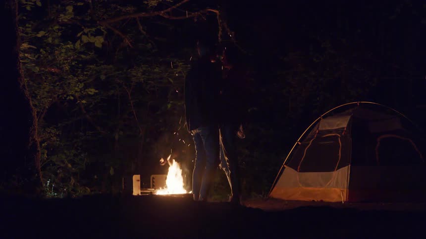 Two people holding each other by a fire at night