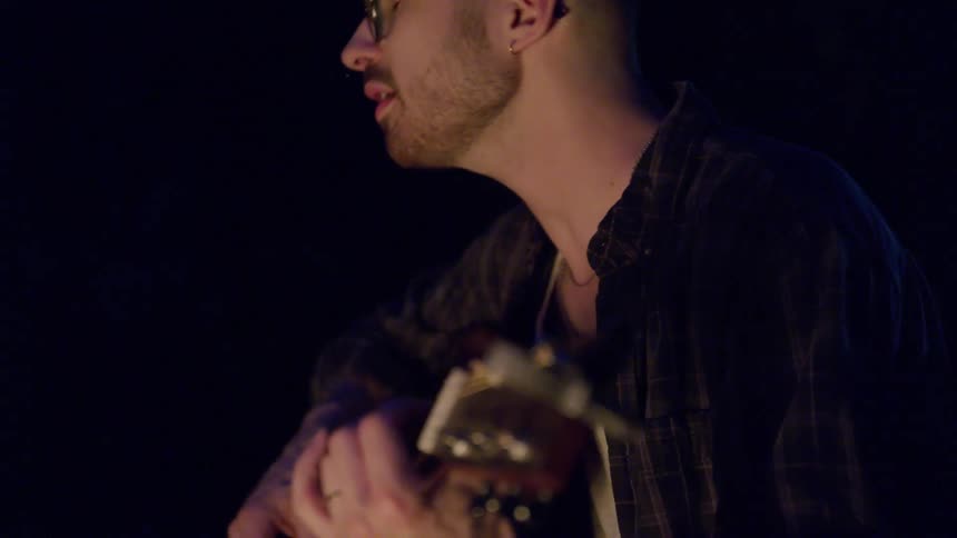 Man plays guitar at night in front of campfire