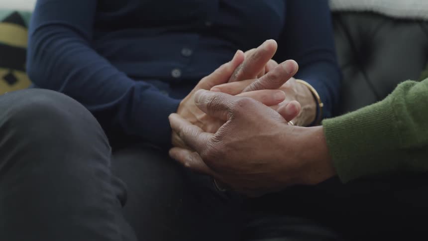 A man and woman hold hands while sitting on a couch