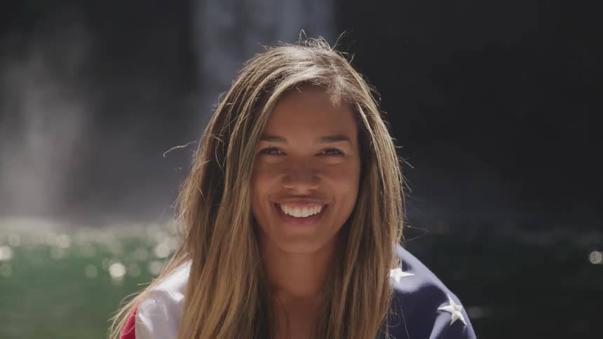 Woman looks at the camera in front of the waterfall and smiles
