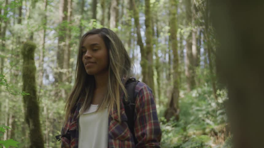 A young woman is walking through a forest of deciduous trees