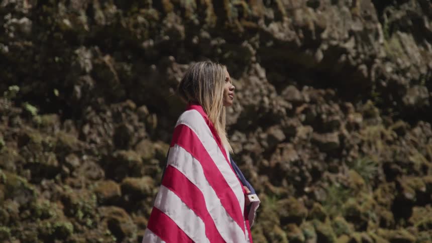 A woman is wrapped in an american flag while standing outside