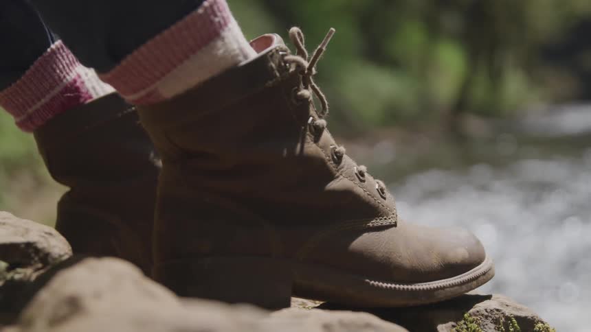 A womens boots on a rock as she sits in front of the water