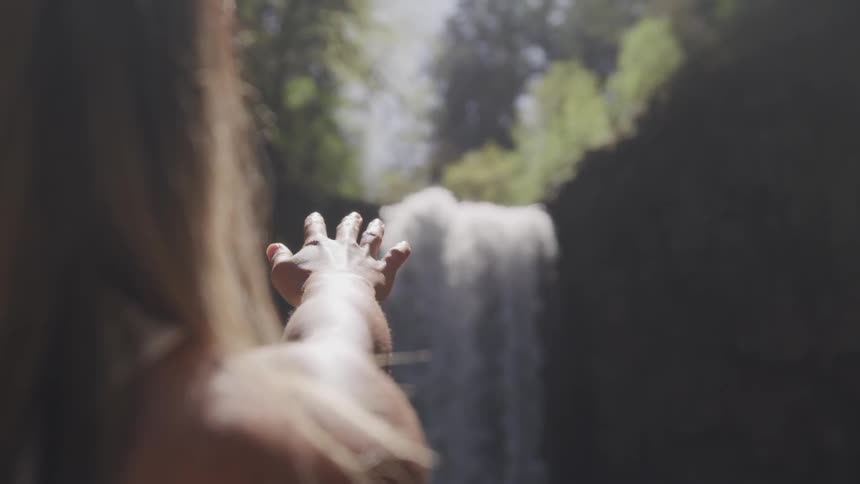 A woman sticking her hand out towards a waterfall