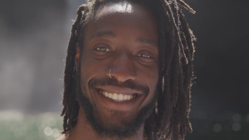 A black man stands by a body of water and grins