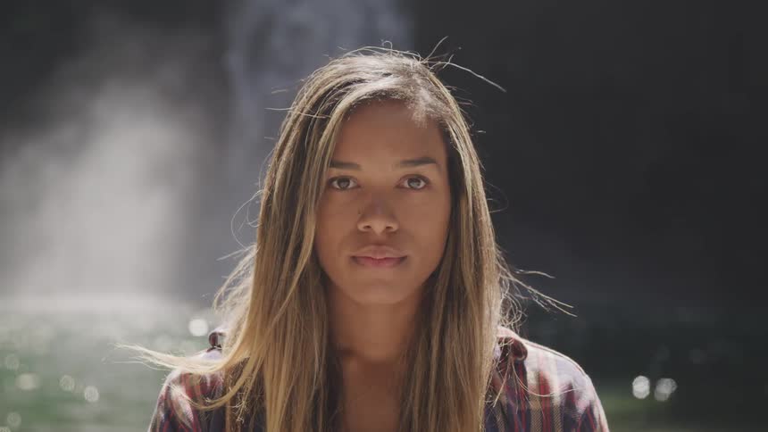 A woman looking into the camera while standing before a waterfall