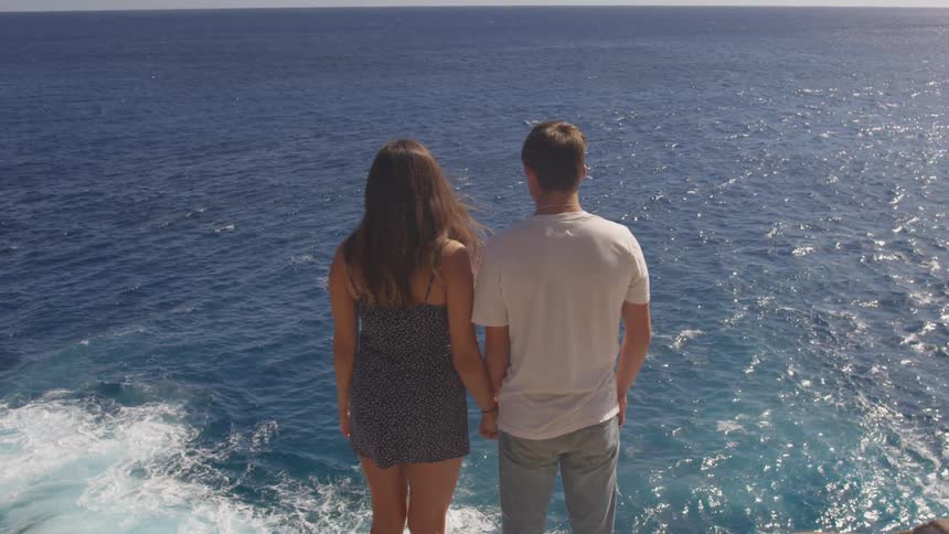 A man and a woman stand on a cliff overlooking the ocean