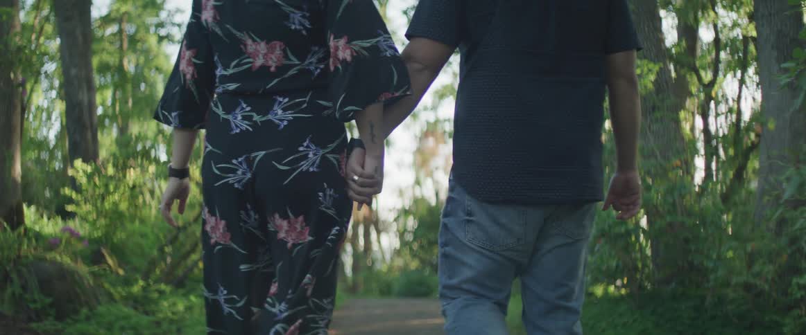 A man and a woman walk down a dirt path in a forest