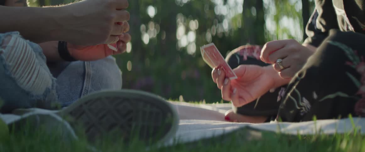 Couple hands playing cards sitting on a blanket on the lawn