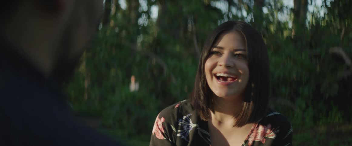 A dark haired woman looks at a man and laughs