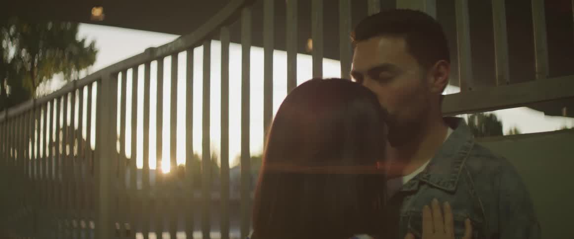 Man leaning on wall kisses woman forehead at sunset