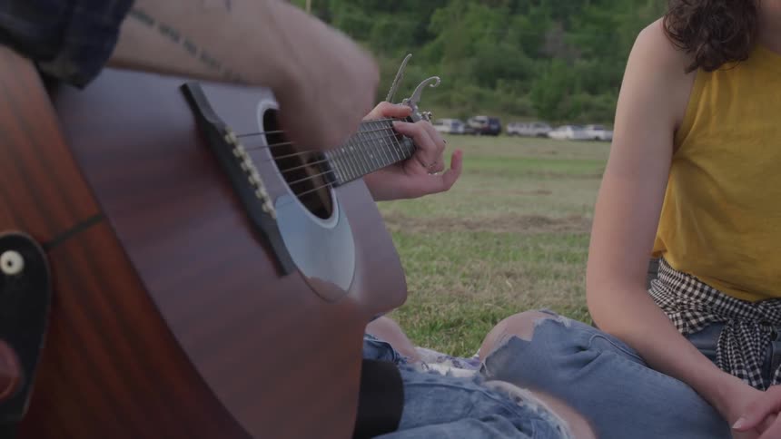 A man plays the guitar while sitting on the ground with a woman