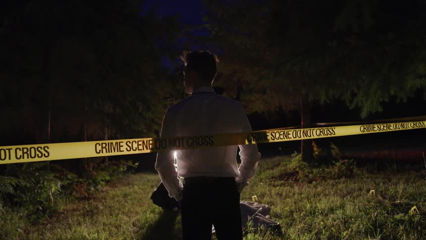 A white man stands just inside a length of crime scene tape and takes in the scene