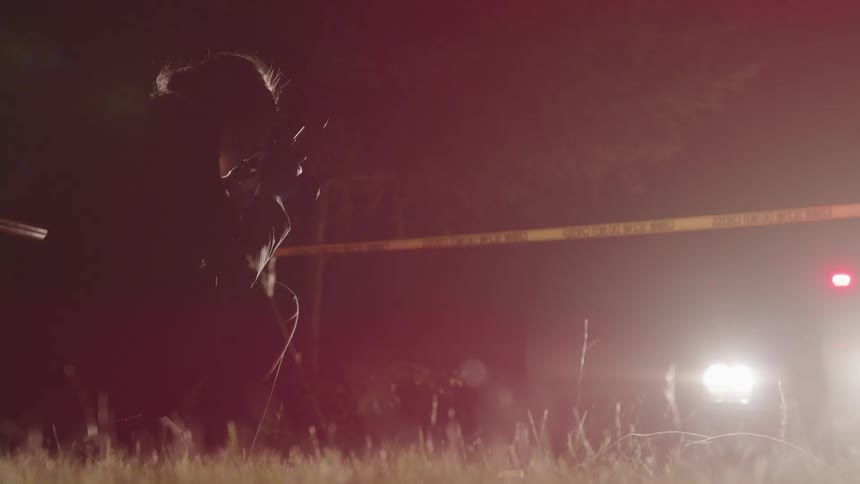 A forensic photographer taking photos of the something on the ground within a police cordon at night