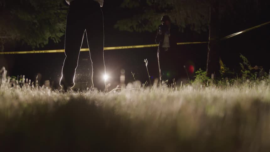 A woman takes pictures at a crime scene as another person stands and watches