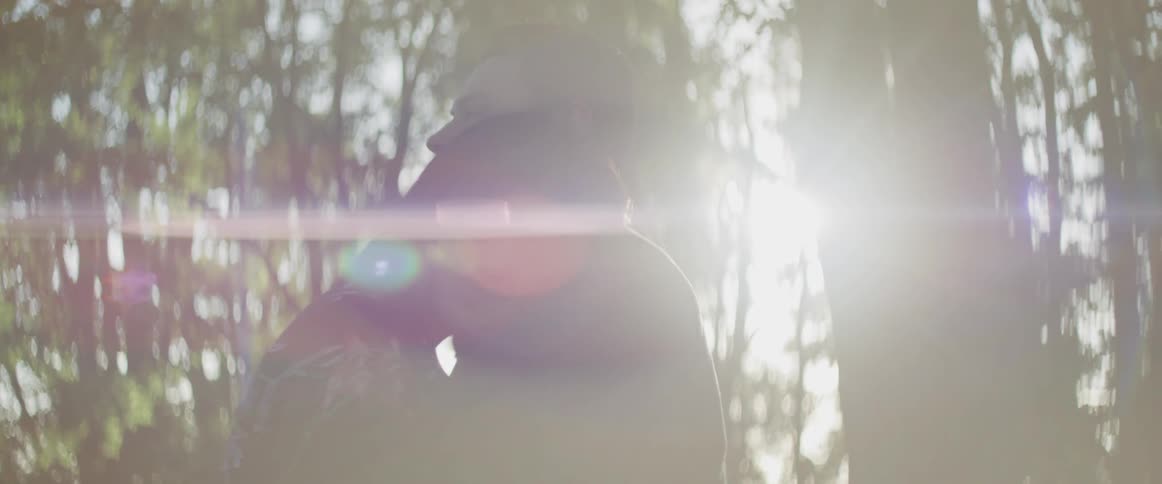 Man and woman cuddle each other while the sun streams through the trees in the forest