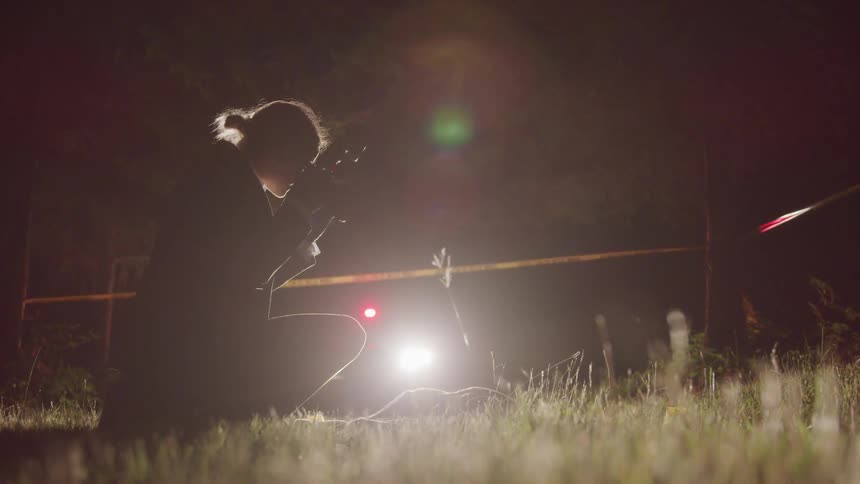 A female investigator kneels over a crime scene and takes some pictures outdoors at night