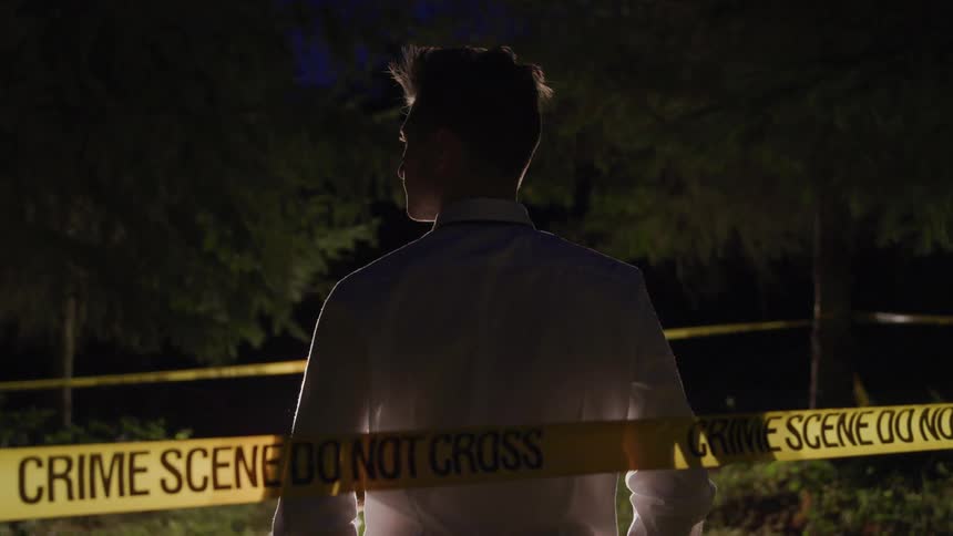 A man stands guard as police investigate a crime scene