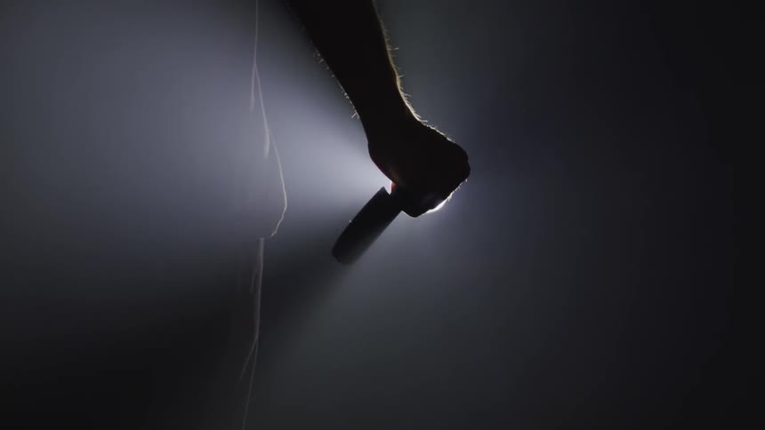 A man stands in front of a bright light holding a knife