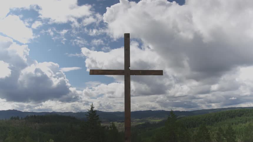 Large wooden cross towers over conifer trees under cloudy sky