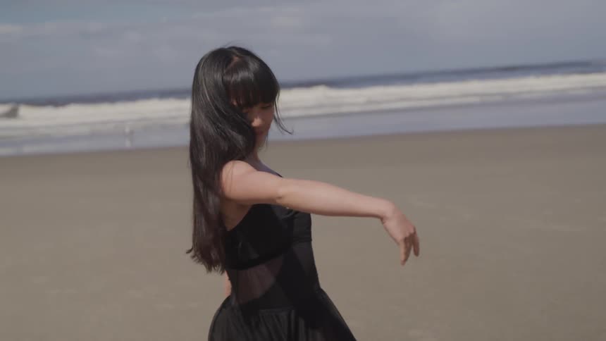 A woman dances and poses on an empty beach
