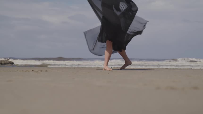 A woman in a black dress is dancing on the beach